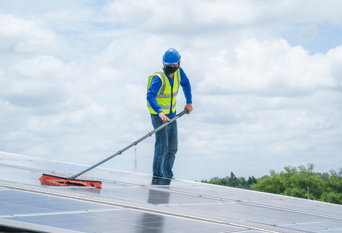 Commercial solar panel maintenance services being completed by a specialist on the roof of a factory.